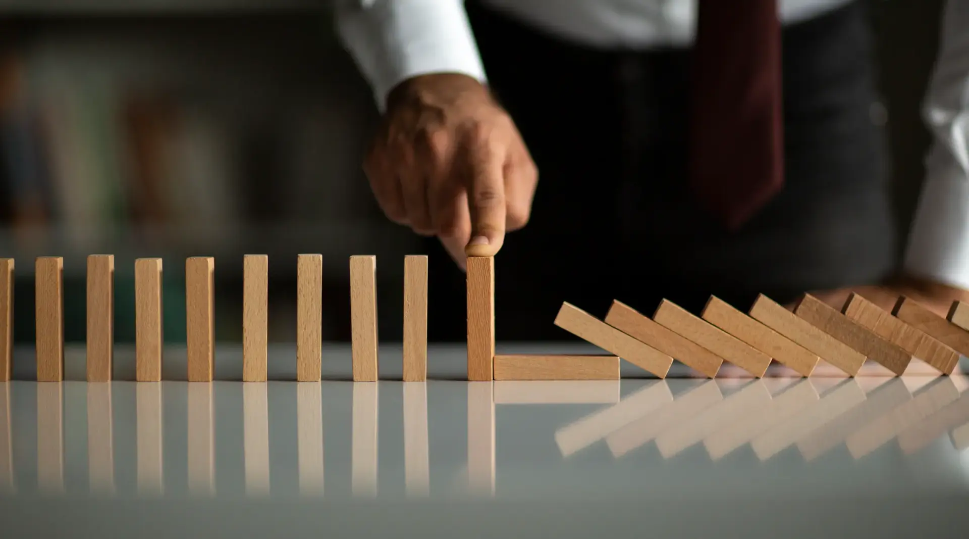A businessman's hand stopping a chain of falling wooden dominoes